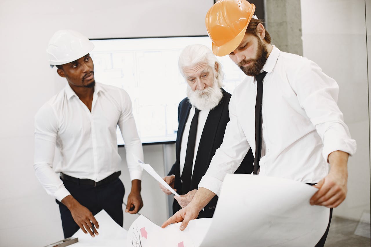 about-01 A diverse team of architects collaborates on a project, examining blueprints together in a modern office setting.